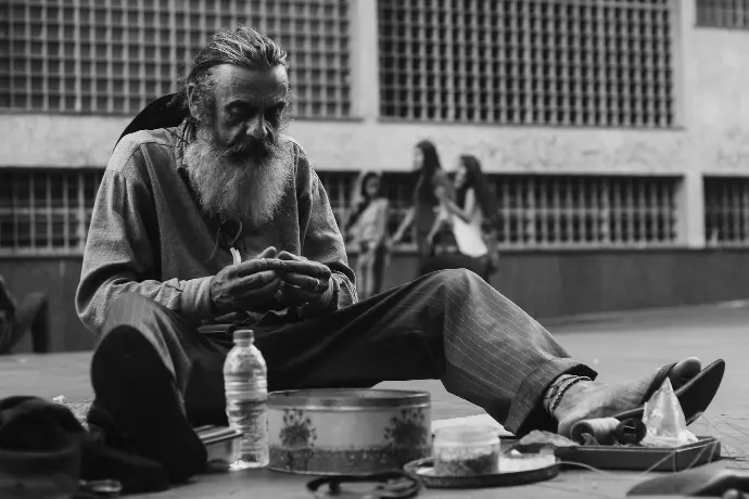 grayscale photo of man sitting on ground with bottle